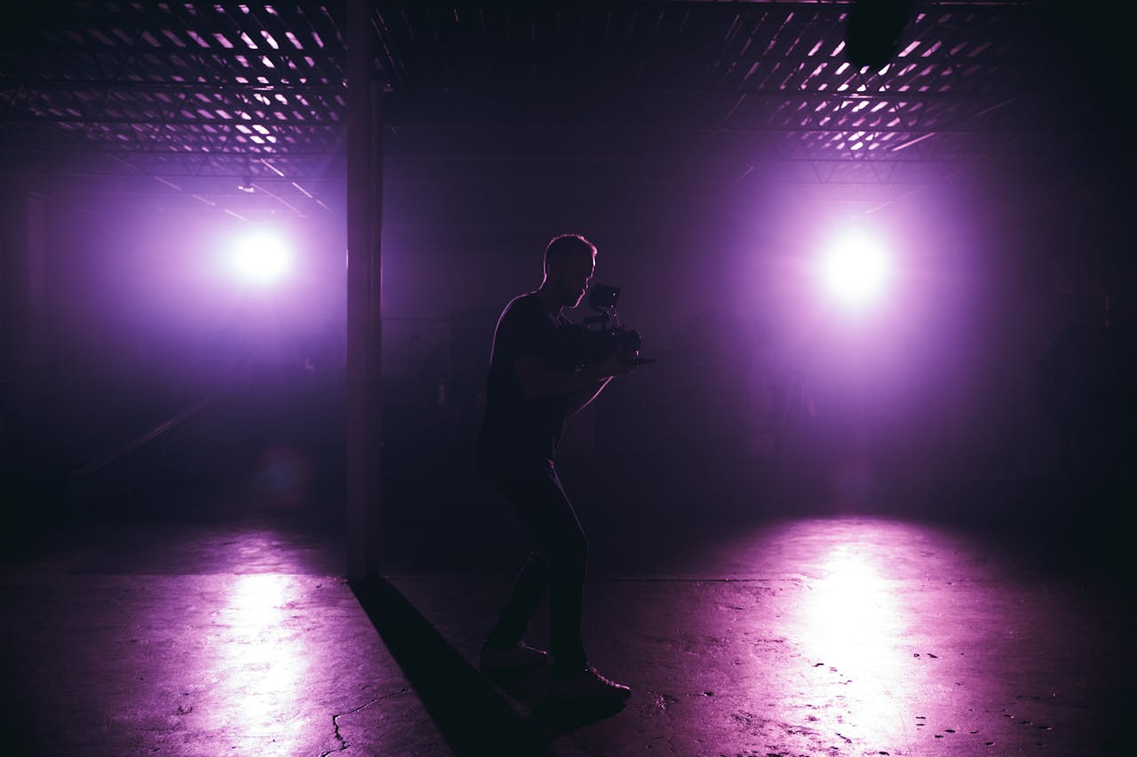 A silhouette of a cameraman filming in an illuminated foggy studio with purple lighting.